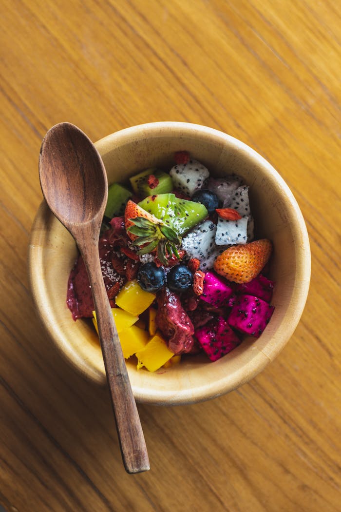 Vibrant mixed fruit bowl with a wooden spoon on a rustic table.
