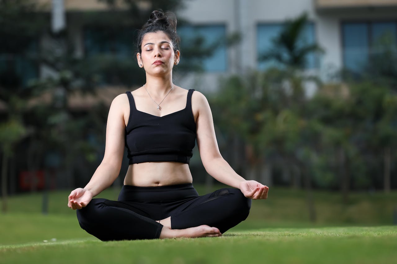 contact-01 A young woman meditating in a park, practicing yoga in a serene outdoor setting.
